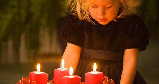 Mädchen blickt von oben auf die vier brennenden Kerzen des Adventskranzes