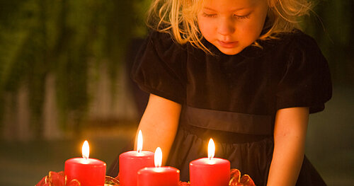Mädchen blickt von oben auf die vier brennenden Kerzen des Adventskranzes