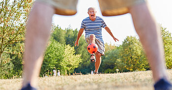 Älterer Mann spielt Fußball mit rotem Ball