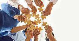 Mehrere Menschen führen Puzzleteile zusammen
