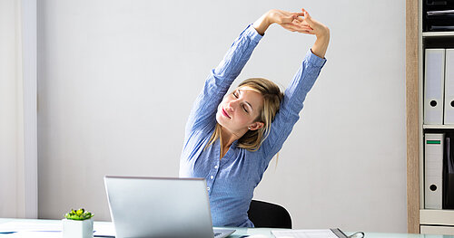Frau streckt Arme während der Arbeit am Laptop