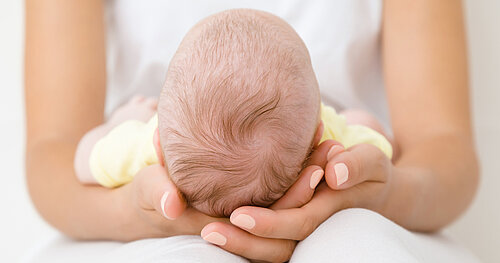 Mutter hält Baby im Arm, Hände schützend unter dem Kopf