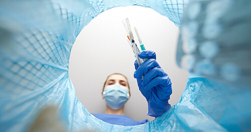 Zum Thema Nachhaltigkeit und Müllaufkommen in der Klink: rankenhausmitarbeiterin mit Maske wirft alte Spritzen in den Mülleimer