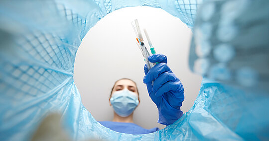 Zum Thema Nachhaltigkeit und Müllaufkommen in der Klink: rankenhausmitarbeiterin mit Maske wirft alte Spritzen in den Mülleimer