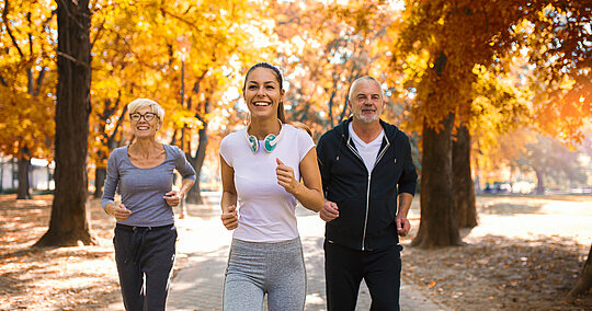 Ältere Frau, jüngere Frau und älterer Mann joggen im herbstlichen Park