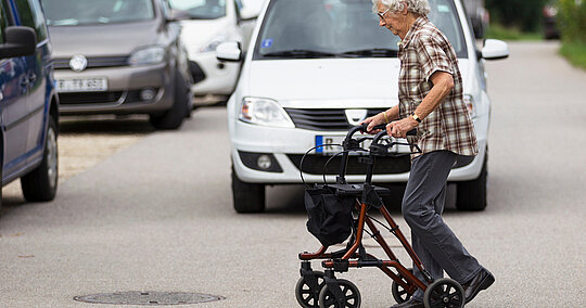 ältere Seniorin mit Rollator überquert die Straße